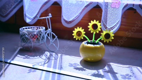 View on a solar powered plastic artificial sunflower moving by the sunlight representing renewable energy source in the window.