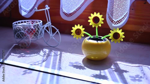 View on a solar powered plastic artificial sunflower moving by the sunlight representing renewable energy source in the window.