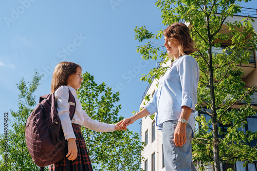 Back to school. Caucasian schoolgirl with a backpack and uniform holds her smiling mother by the hand in the street before going to school.