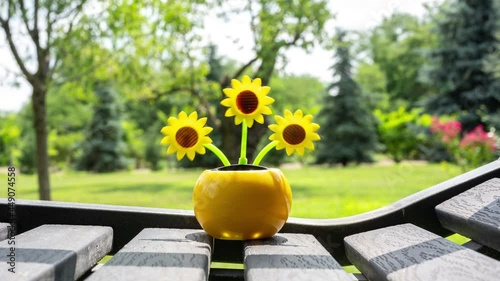 Time-lapse view on a solar powered plastic artificial sunflower moving by the sunlight representing renewable energy source on a bench in the garden.