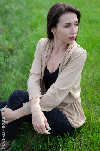 beautiful brunette woman sitting on green grass.