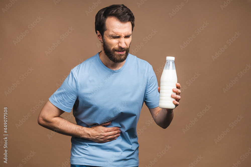 Young man in pain holding his hurting stomach isolated on beige background. Abdominal pain. Lactose milk intolerance. Young man in pain holding his hurting stomach isolated on beige background. Abdominal pain. Lactose milk intolerance.