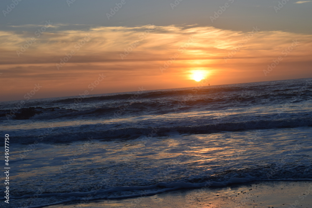 orange sun setting on the west coast horizon with a view of the ocean tide