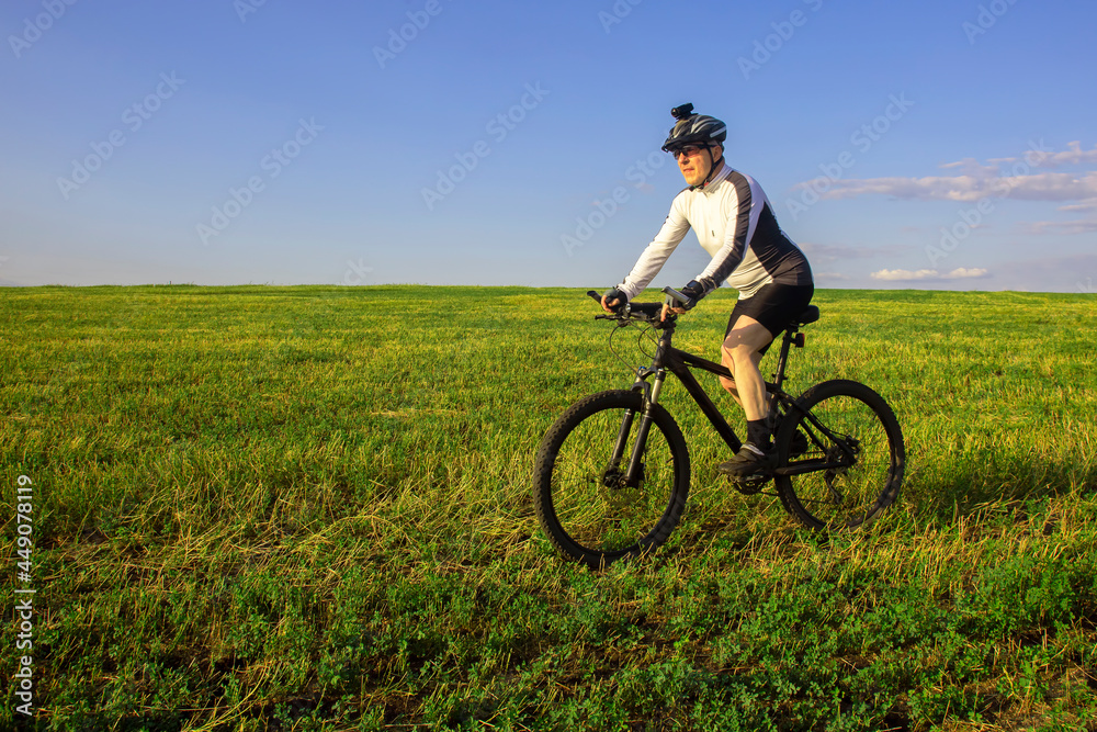 cyclist on bike rides along the fields of wheat in the sunlight