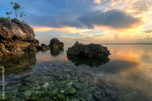 a body of water with rocks and tree at sunrise