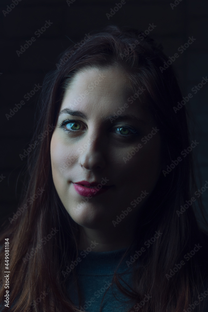 Fototapeta premium mujer con ojos verdes y labios rojos posando con luz lateral, retrato con luz lateral, rostro femenino con la mitad de la cara iluminada y la otra mitad con sombra