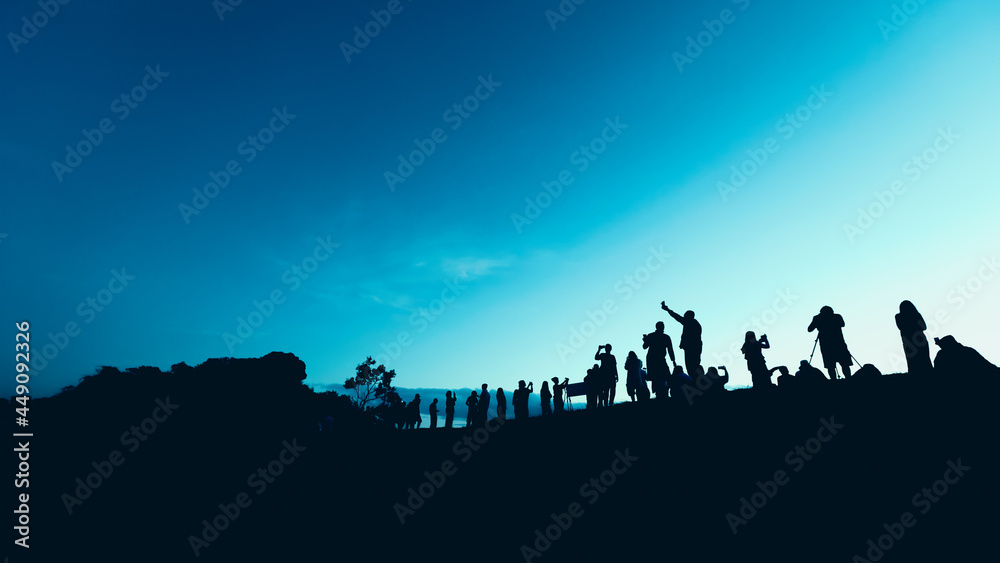 Silhouettes of tourist crowd waiting for the sunrise and doing activity, taking a photo, selfie with nature on the hill at viewpoint