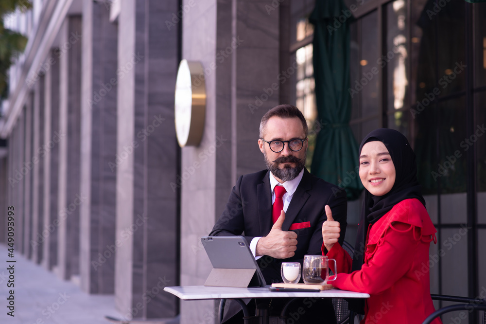 businessman caucasian and businesswoman Muslim working outdoor in the front of a coffee shop.