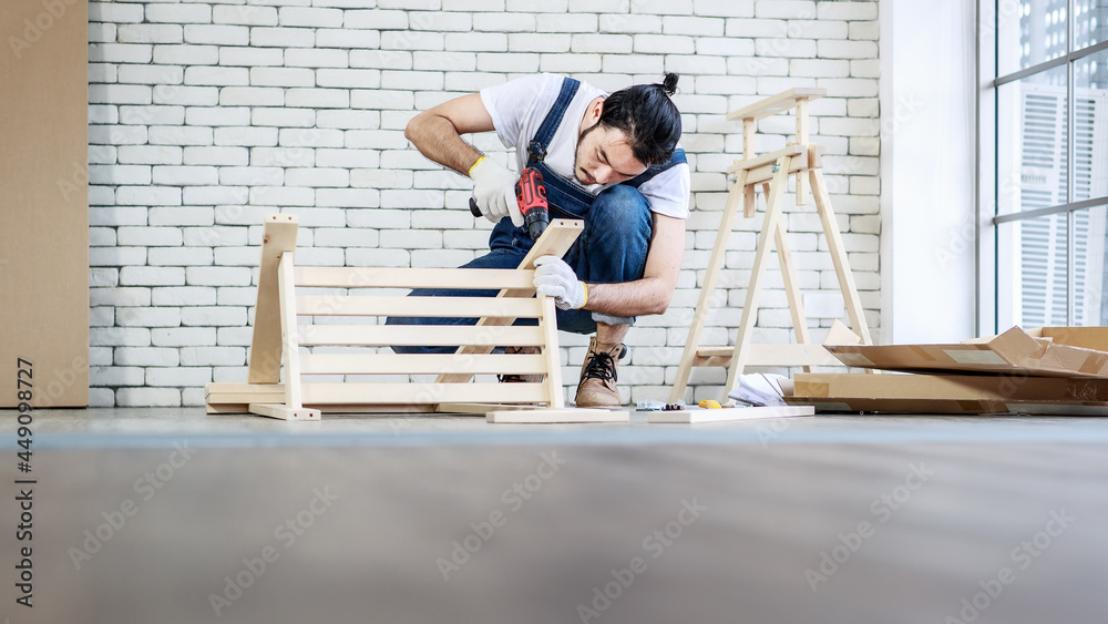 Young Asian hipster man working as handyman, assembling wood table with equipments, concept for home diy and self service and hobby
