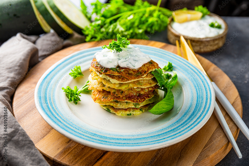Zucchini pancakes with herbs and sour cream on a blue plate close-up. Vegetarian dish