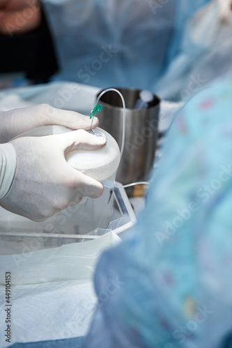 Surgeons during surgery with breast implants in their hands  installation of breast implants  surgery. Plastic surgery  breast correction  mammoplasty.