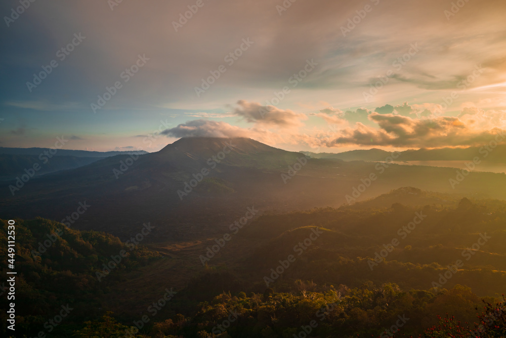Beautiful mountain landscape during sunrise. Hills, Batur volcano and lake. Scenic panoramic view. Colorful sky with clouds. Foggy morning. Kintamani, Bali