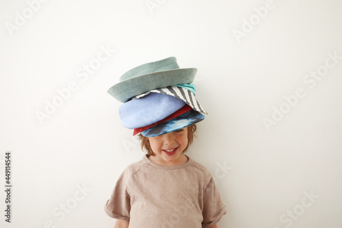 Smiling boy wearing t shirt and various headwear standing against white background and looking at camera
