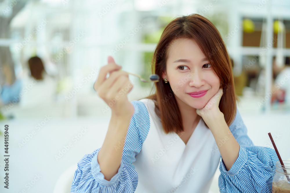 A beautiful Asian portrait is taking a spoonful of cakes on the table and eating them with happy eyes and expressions in the bakery. A beautiful Asian portrait is taking a spoonful of cakes on the table and eating them with happy eyes and expressions in the bakery.