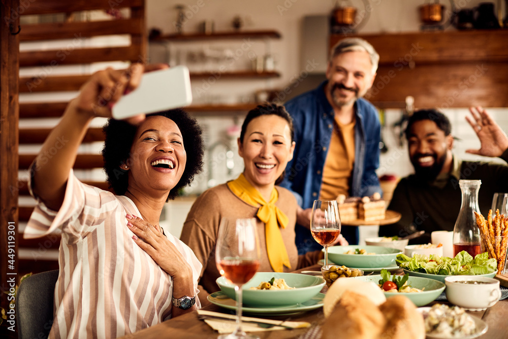 Cheerful multi-ethnic group of friends take selfie during meal at dining table.