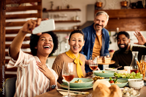 Cheerful multi-ethnic group of friends take selfie during meal at dining table.