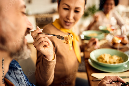 Close-up of woman feeds her husband with pasta at dining table.