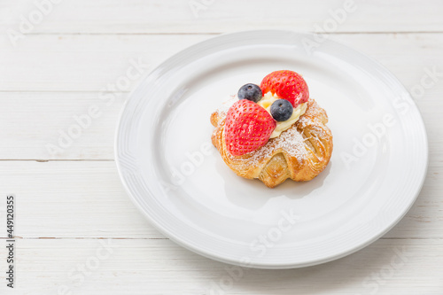 Fresh croissant with whipped cream and strawberries blueberries on a white plate