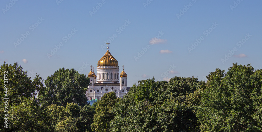 The Cathedral of Christ the Savior with a golden dome among the green foliage of trees against a bright blue sky on a sunny summer day in Moscow Russia and a space for copying in Moscow