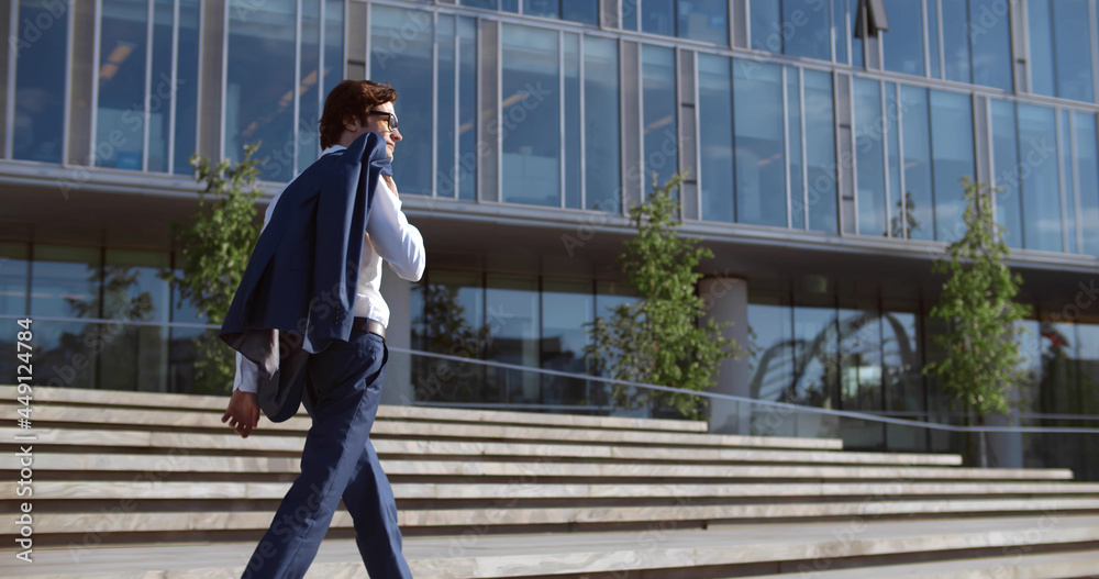 Side view of successful young businessman walking stairs outside office building