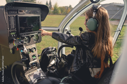 Preteen girl in headset pointing at dashboard in helicopter cockpit photo