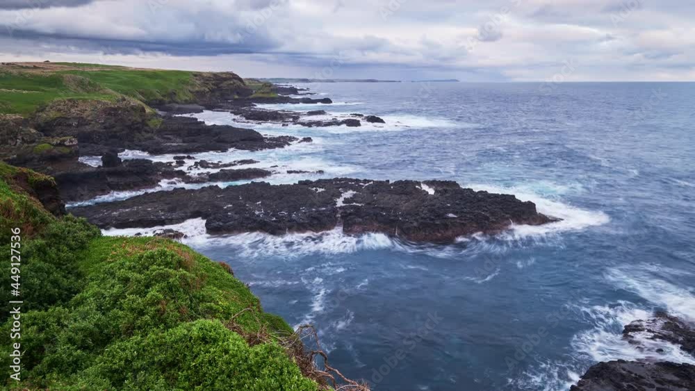 Time lapse of ocean waves breaking against small rocky islands surrounded by tall cliffs covered in beautiful green foliage and deep blue sea. In the background dark storm clouds gather overhead. Time lapse of ocean waves breaking against small rocky islands surrounded by tall cliffs covered in beautiful green foliage and deep blue sea. In the background dark storm clouds gather overhead.