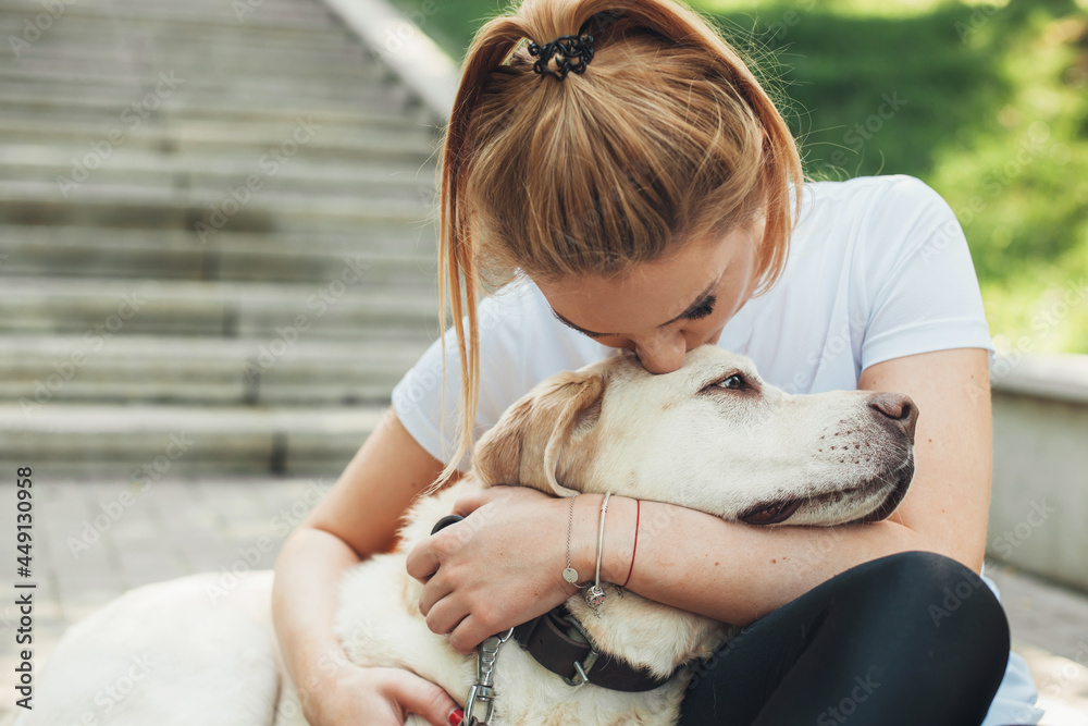 Caucasian woman is embracing her labrador kissing him during a walk in the park Caucasian woman is embracing her labrador kissing him during a walk in the park