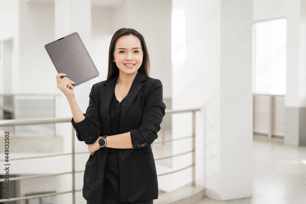 Portrait stock photo of a confident cheerful Asian businesswoman professional in black business suit using a digital tablet standing in the office building representing business oriented concept Portrait stock photo of a confident cheerful Asian businesswoman professional in black business suit using a digital tablet standing in the office building representing business oriented concept