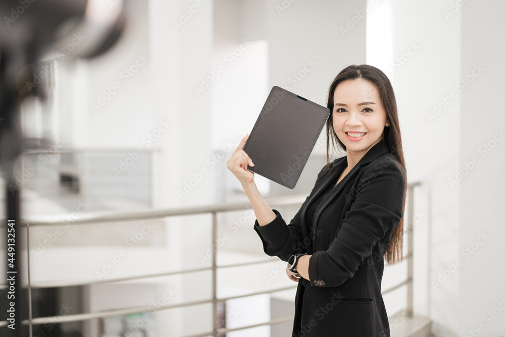 Portrait stock photo of a confident cheerful Asian businesswoman professional in black business suit using a digital tablet standing in the office building representing business oriented concept Portrait stock photo of a confident cheerful Asian businesswoman professional in black business suit using a digital tablet standing in the office building representing business oriented concept