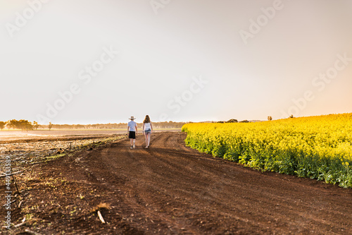 Young boy and girl walking on dirt road on farm next to canola field at sunset photo