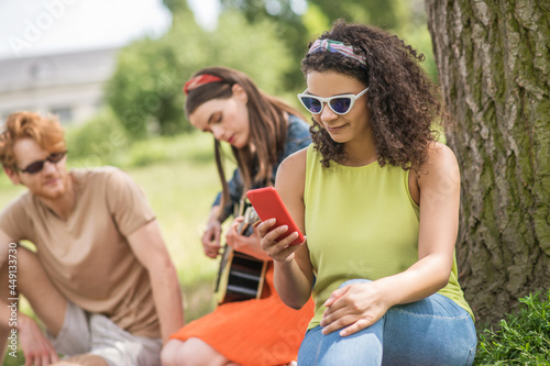 Girl looking into smartphone girlfriend with guitar and boyfriend © zinkevych