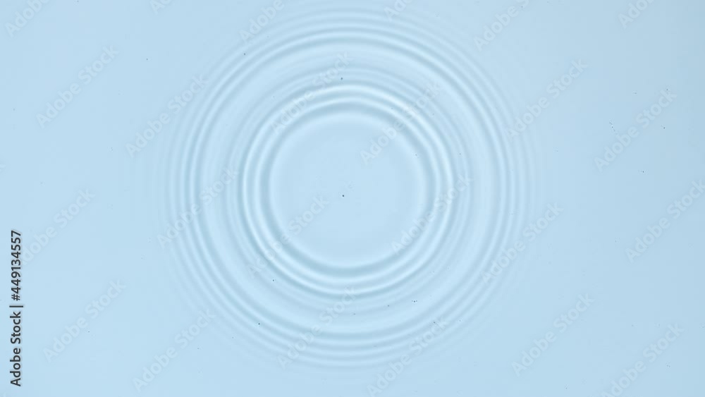 White drop falls down creating circles on water surface on pale blue background | Background shot for skin care cosmetics commercial