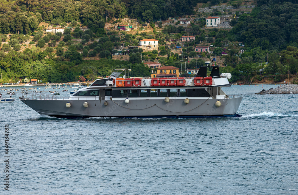Empty white ferry boat in motion in front of the Palmaria Island (Isola di Palmaria) seen from Porto Venere or Portovenere town, UNESCO world heritage site, Gulf of La Spezia, Liguria, Italy, Europe.