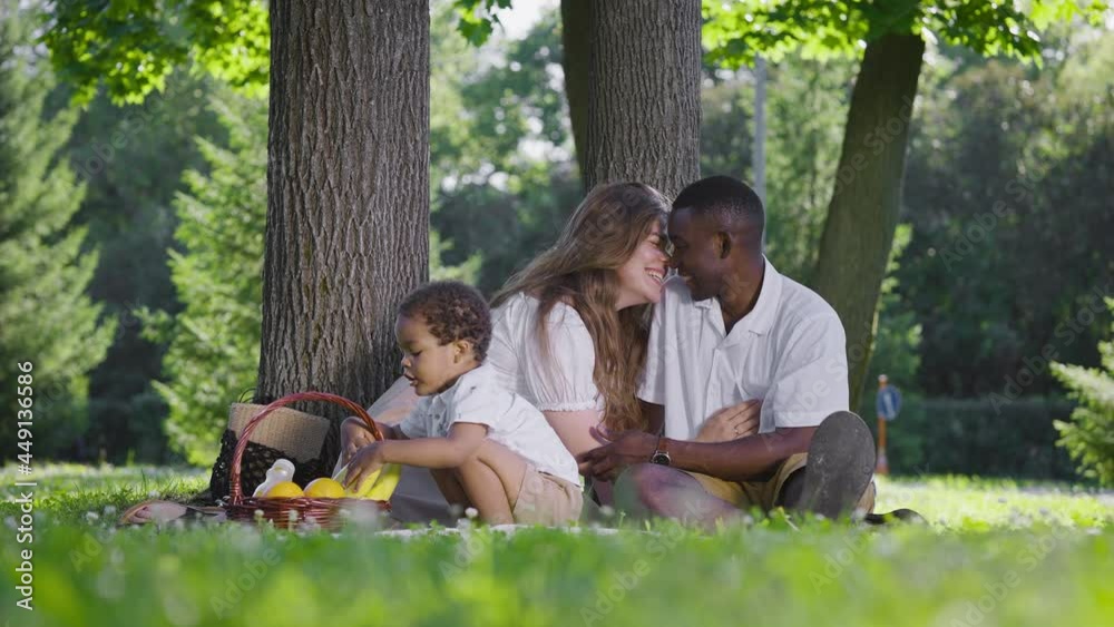 A cute multicultural family had a picnic in the park. Mom, dad and son sat on a blanket, next to a basket of food. A cute multicultural family had a picnic in the park. Mom, dad and son sat on a blanket, next to a basket of food.