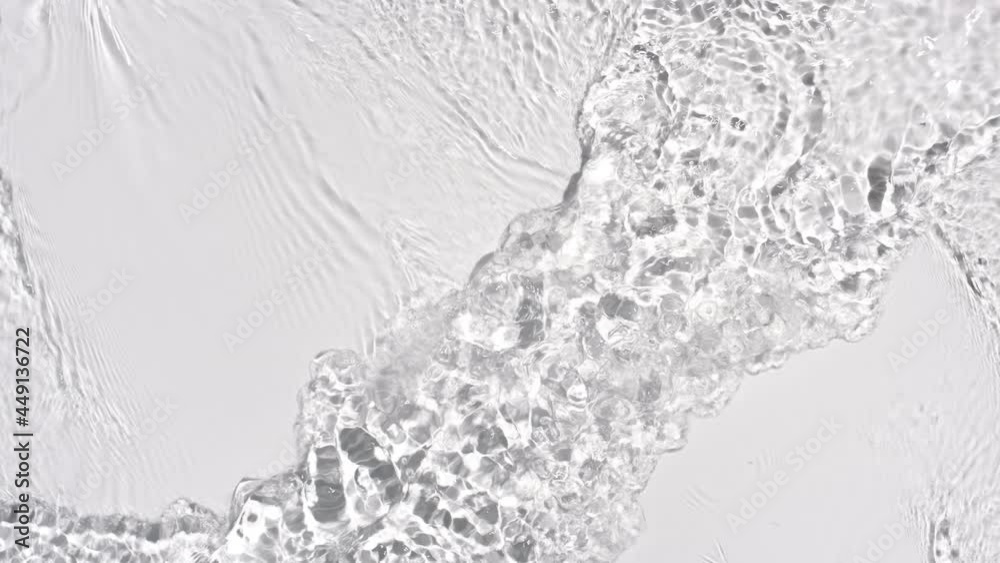 Water flows from opposite sides creating waves, ripples and concentric circles on pale grey background | Background shot for skin care cosmetics with hyaluronic acid commercial