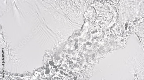 Water flows from opposite sides creating waves, ripples and concentric circles on pale grey background | Background shot for skin care cosmetics with hyaluronic acid commercial photo