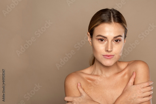 Young lovely woman is touching her shoulder. Beautiful face of young woman with clean fresh skin close up on beige background. Skin care face . Cosmetology