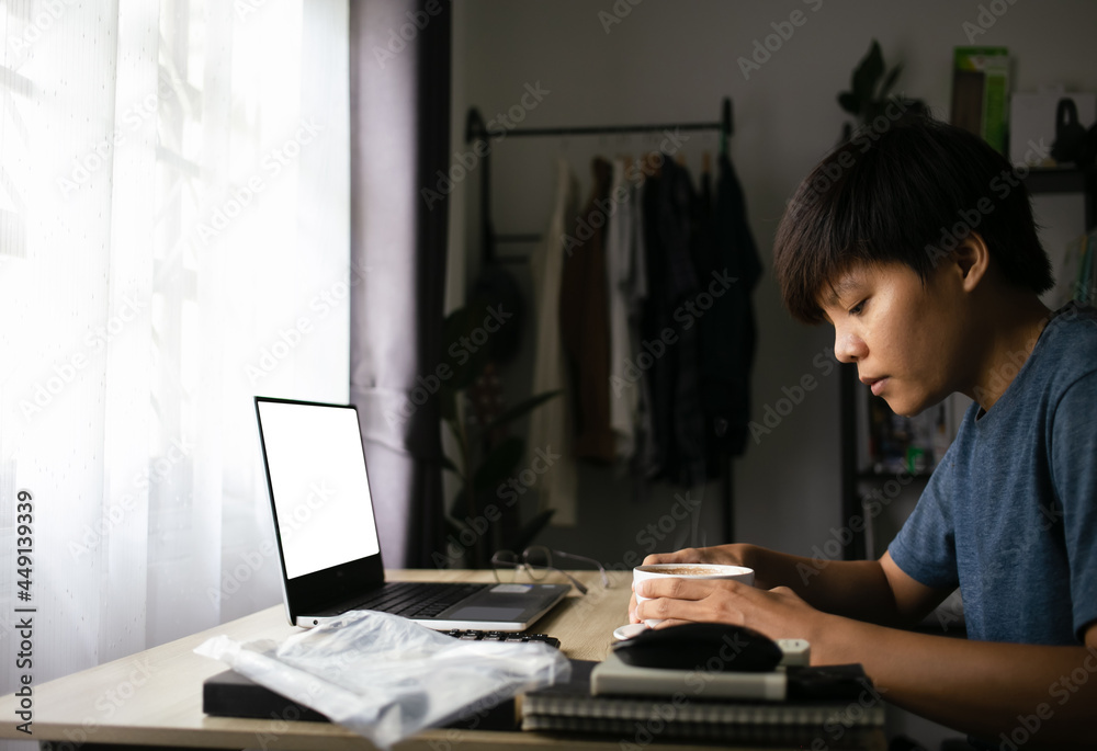 Asian young man holding a cup of coffee ready start to hard work with mock-up white screen laptop device workspace desktop working at the home office in the morning Asian young man holding a cup of coffee ready start to hard work with mock-up white screen laptop device workspace desktop working at the home office in the morning