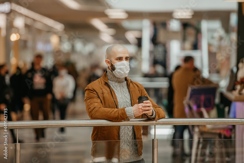 A man in a face mask is holding a cup of coffee in the shopping center.