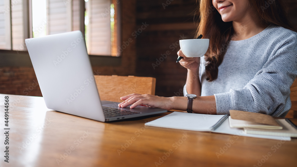 Closeup image of a young woman drinking coffee while working on laptop computer Closeup image of a young woman drinking coffee while working on laptop computer