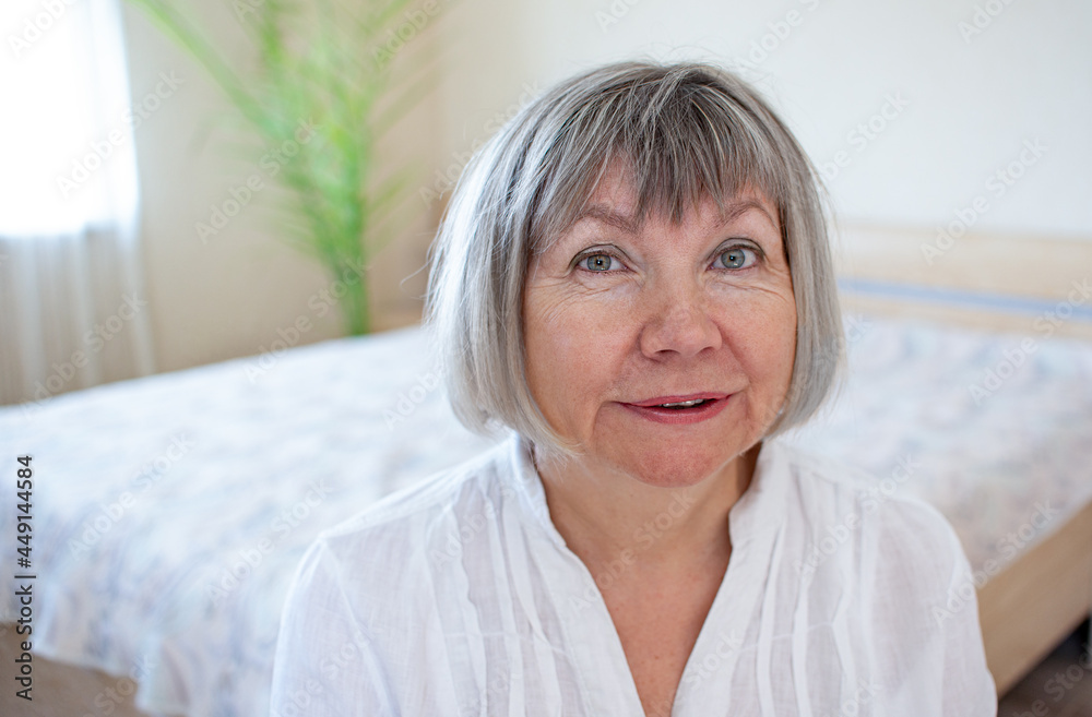 Happy senior woman with gray hair relaxing smiling is looking at the camera in her home in the bedroom Happy senior woman with gray hair relaxing smiling is looking at the camera in her home in the bedroom