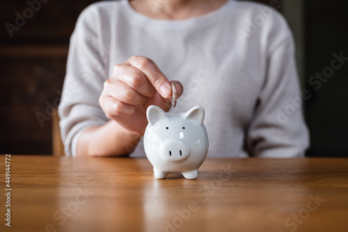 Closeup image of a woman putting coins into piggy bank for saving money concept