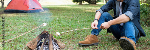 Man warm near campfire in forest and marshmallow on skewers.