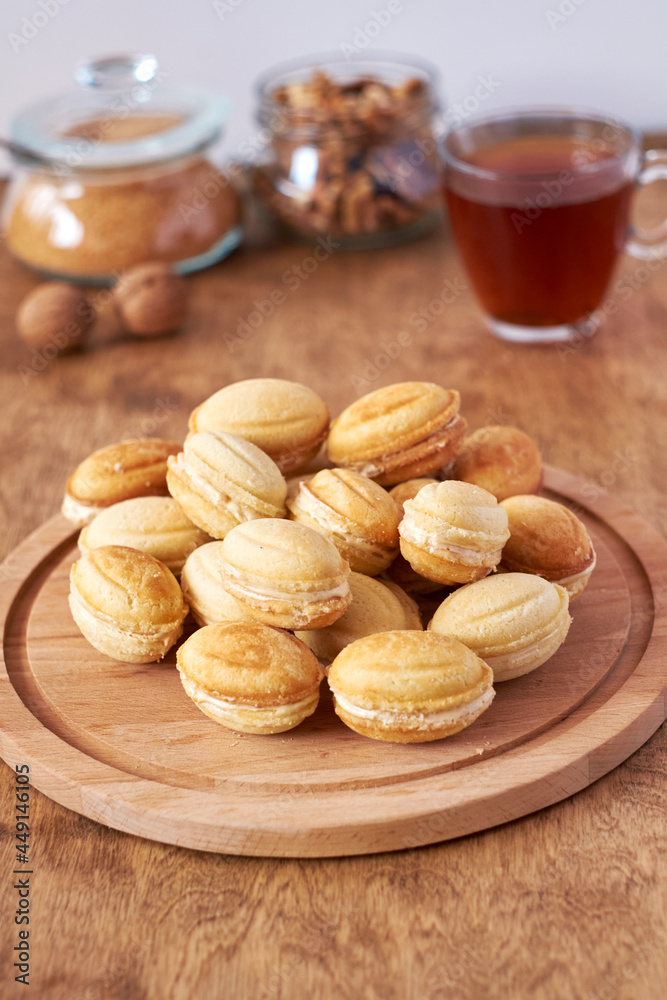Walnut cookies with cream filling. Cookies on a wooden board. Side view, white and wood background. Tea. Walnut cookies with cream filling. Cookies on a wooden board. Side view, white and wood background. Tea.