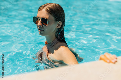 young tanned woman in sunglasses, in the outdoor pool, woman in a swimsuit sunbathing in the pool, Happy woman relaxing in the pool © Shopping King Louie