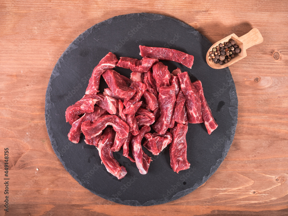 Raw cuts of beef for roast and beef stroganoff on a slate round board