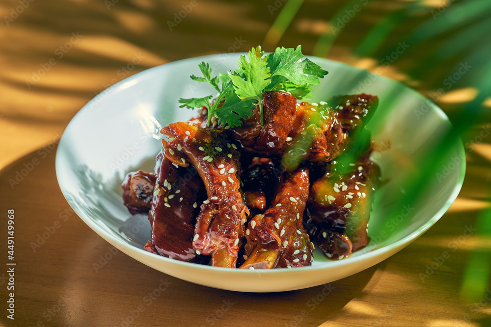 Pork ribs in sweet and sour sauce with cilantro, sesame seeds and Sichuan pepper in a white bowl. Chinese cuisine Pork ribs in sweet and sour sauce with cilantro, sesame seeds and Sichuan pepper in a white bowl. Chinese cuisine