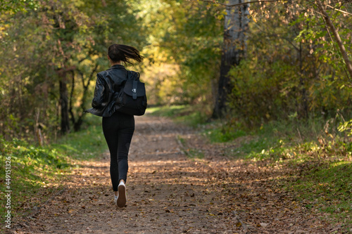 Girl runs along the park alley. Woman runs away from someone in the park.