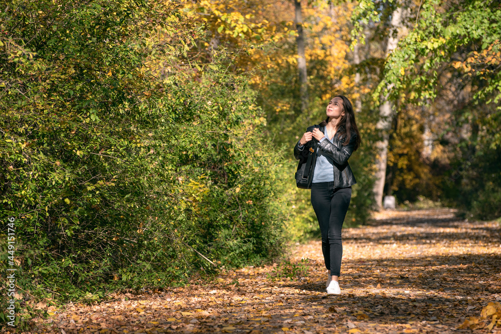 Young beautiful woman walks along the alley of an autumn park and enjoys a warm day. Lonely girl walk through the forest
