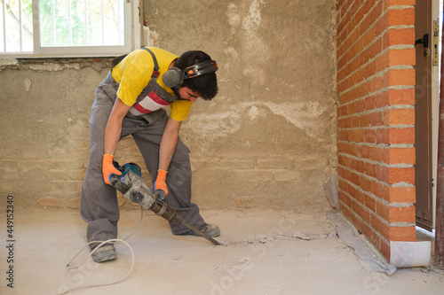 Young builder breaking up a house floor with a jackhammer.